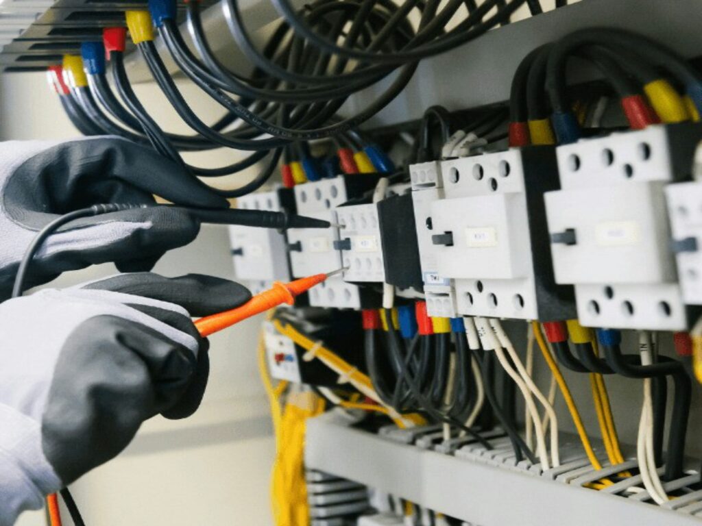 Ein Schaltschrank wird von zwei Händen mit Phasendrehern angeschlossen.