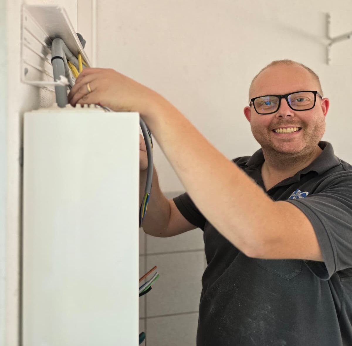 Kontakt Lachender Geschäftsführer Simon Hofbauer, der seine Hände bei der Arbeit auf einen Schaltschrank legt.