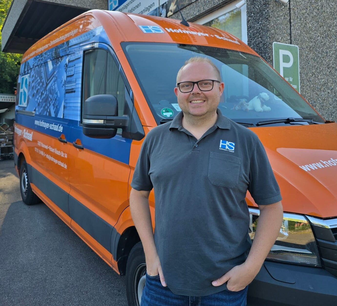 Geschäftsführer Simon Hofbauer vor dem firmeneigenen Fahrzeug in den Unternehmensfarben Orange und Blau.