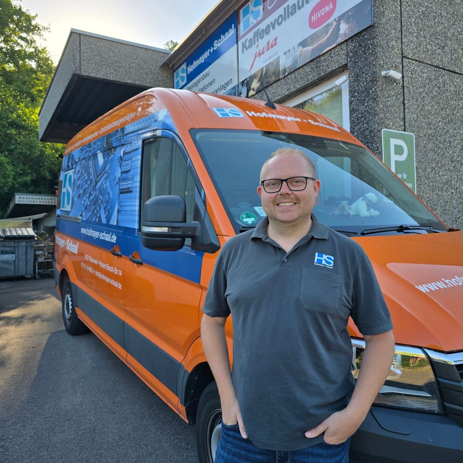 Geschäftsführer Simon Hofbauer vor dem firmeneigenen Fahrzeug in den Unternehmensfarben Orange und Blau.